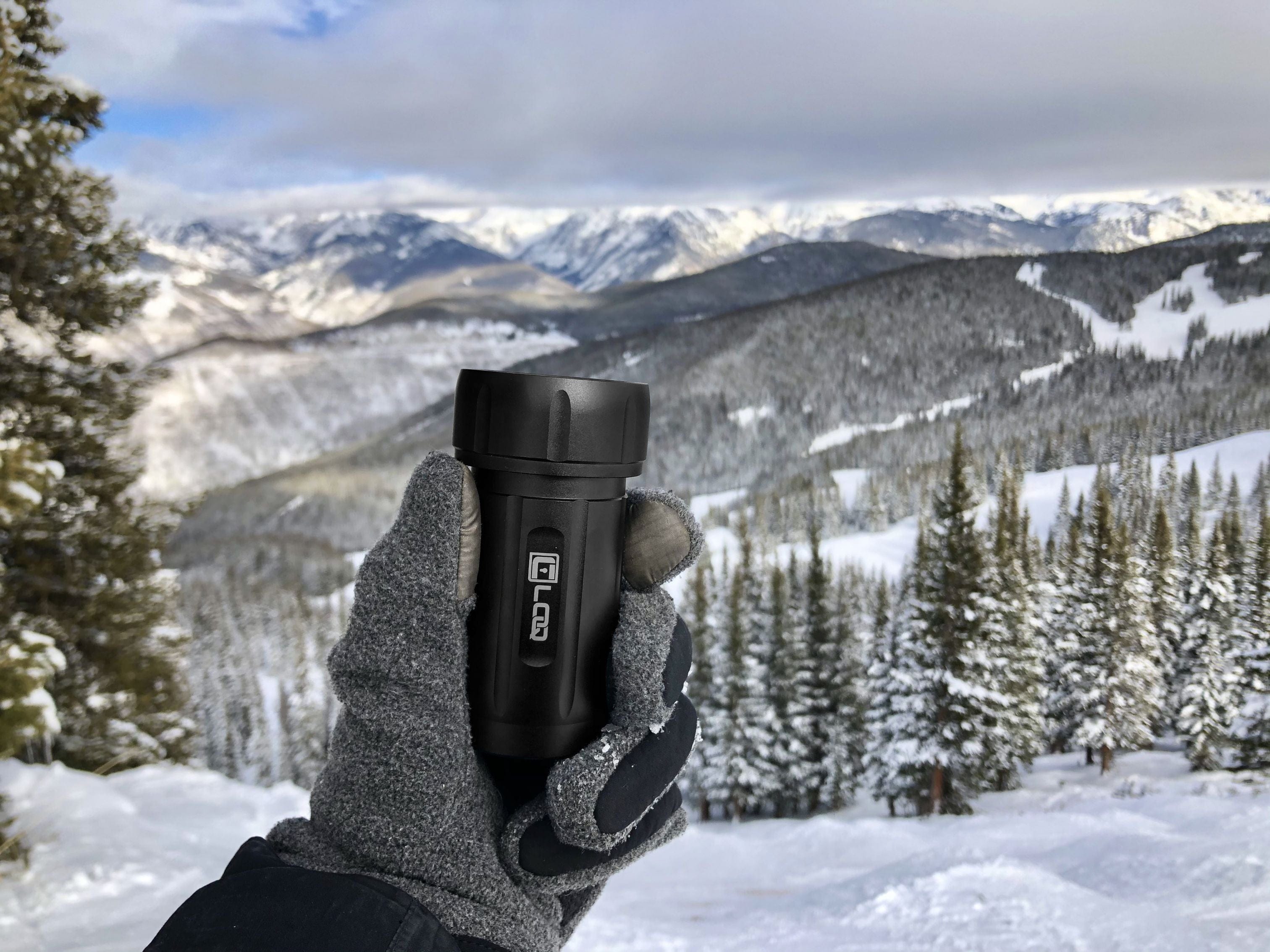 A hand holds the Zytel Black Premium 120CC Storage Canister against a snowy mountain backdrop under overcast skies.