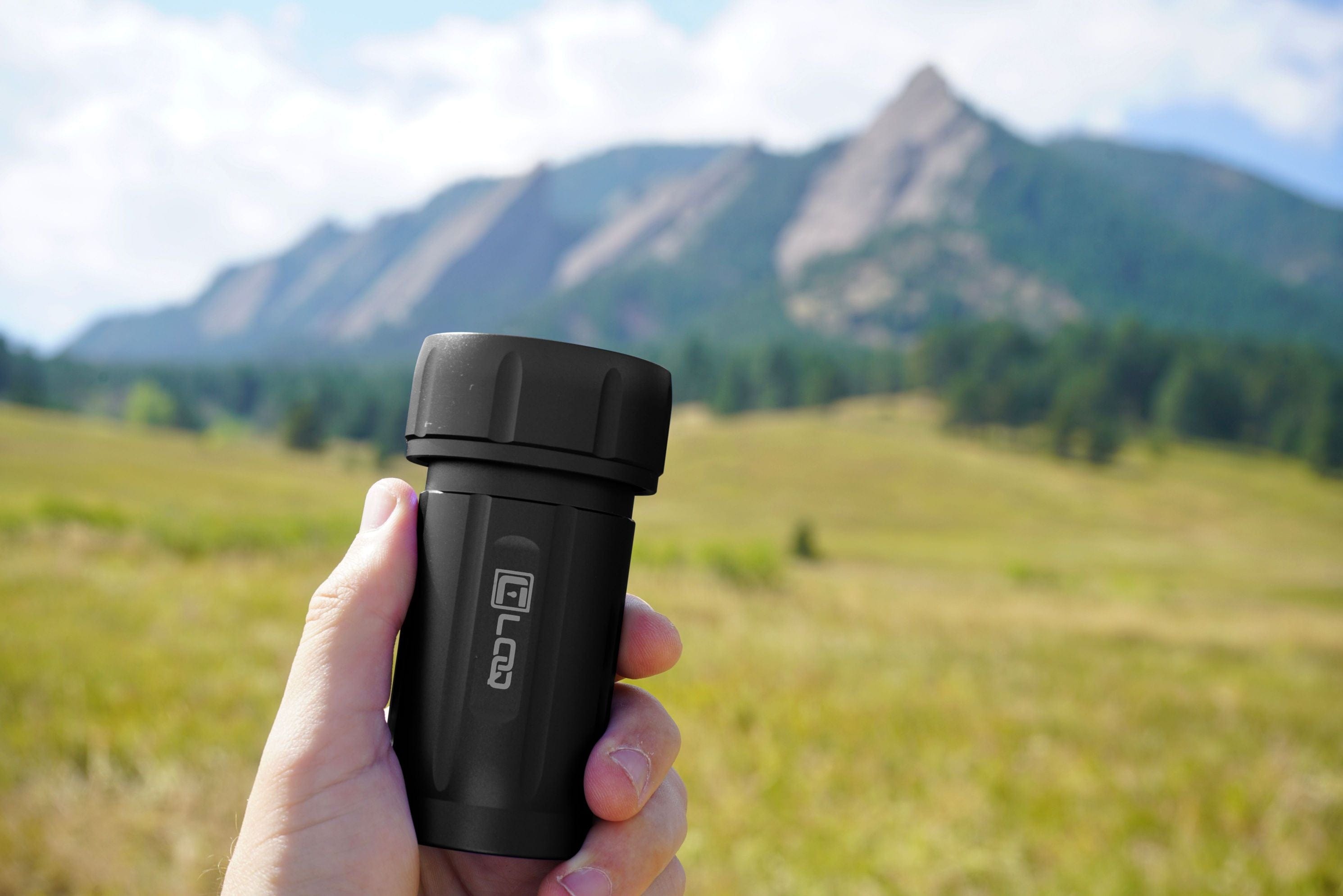 A hand holds the Zytel Black Premium 120CC Storage Canister against a backdrop of rolling green hills and a hazy mountain range.