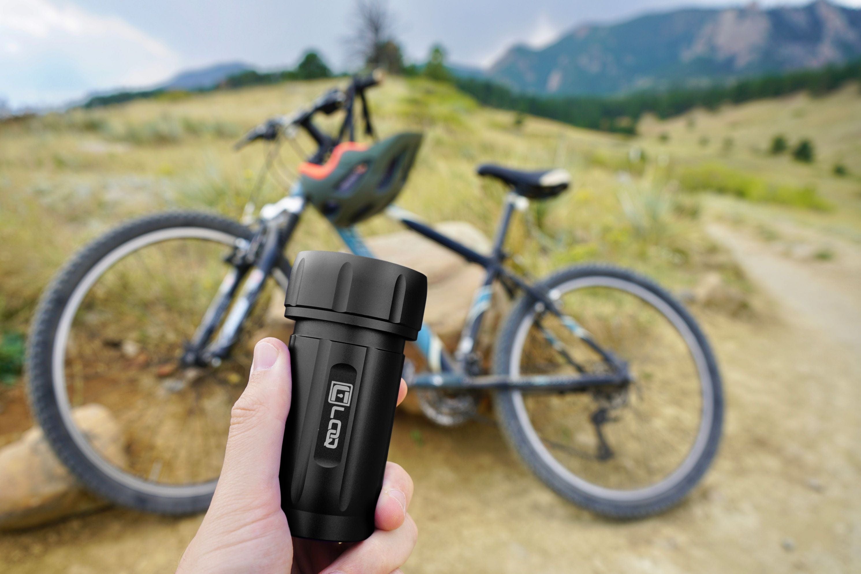 A hand holds the Zytel Black Premium 120CC Storage Canister against a blurred background of a bicycle and hillside.