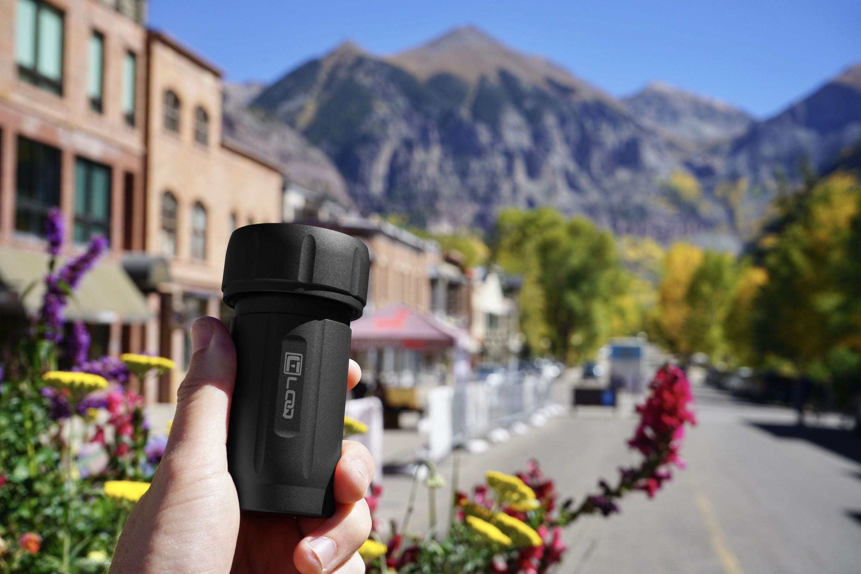A hand holds the Zytel Black Premium 120CC Storage Canister with a tan cap, set against a blurred mountainous background.