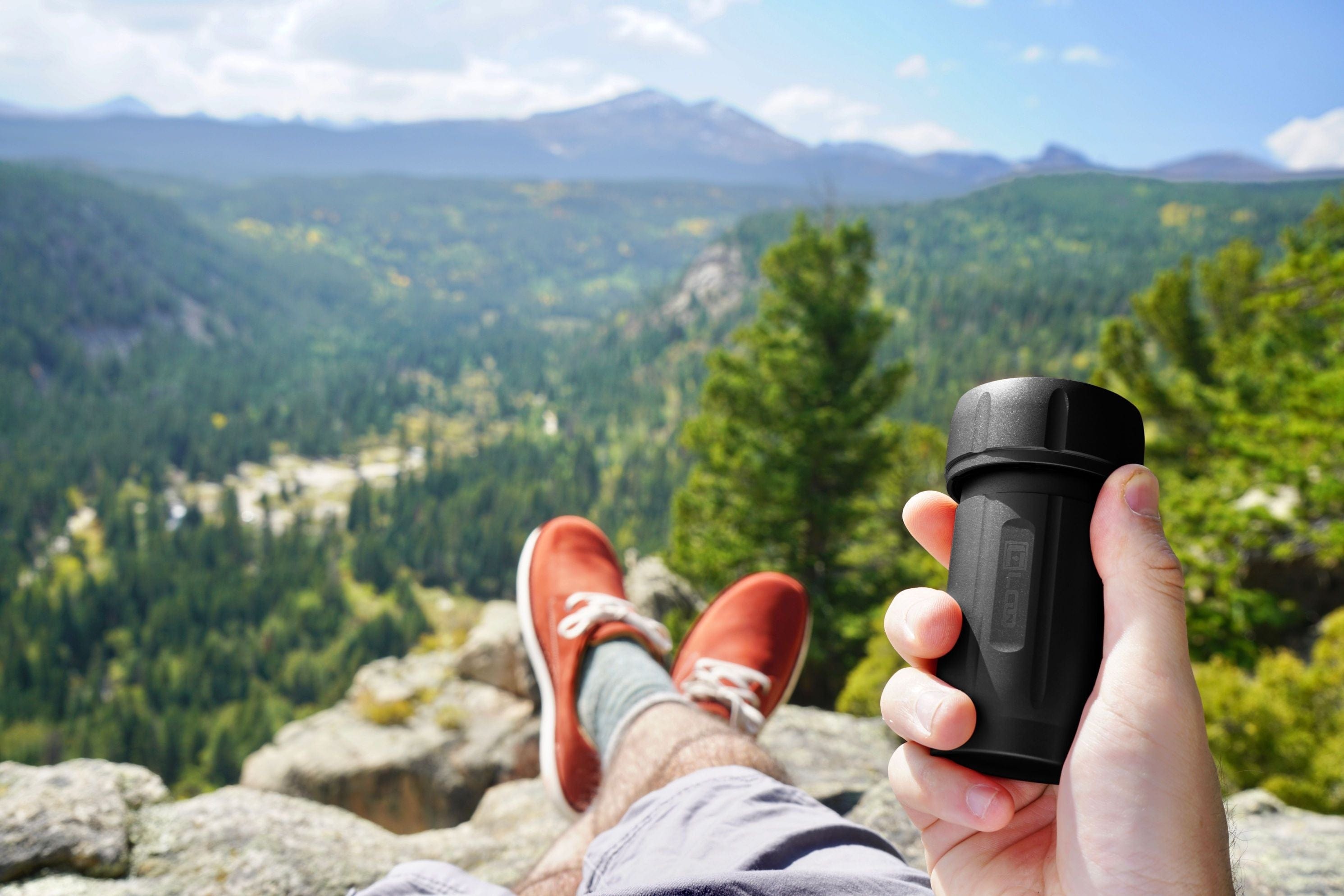 A first-person view shows a hand holding the Zytel Black Premium 120CC Storage Canister against a backdrop of forested hills.