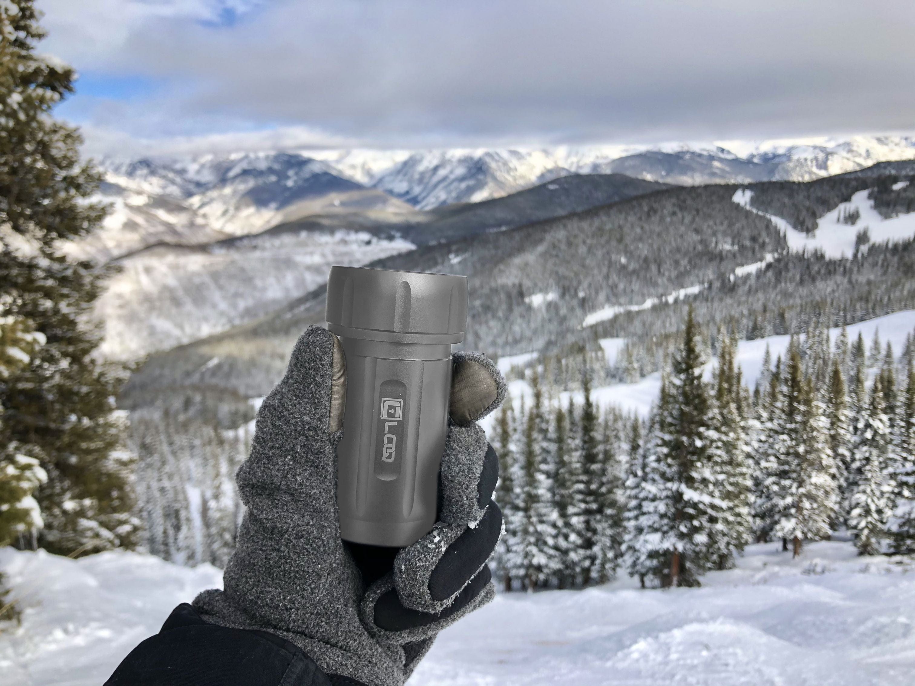 A hand holds the Zytel Gray Premium 120CC Storage Canister against a blurred mountain backdrop, highlighting its sleek cylindrical shape.