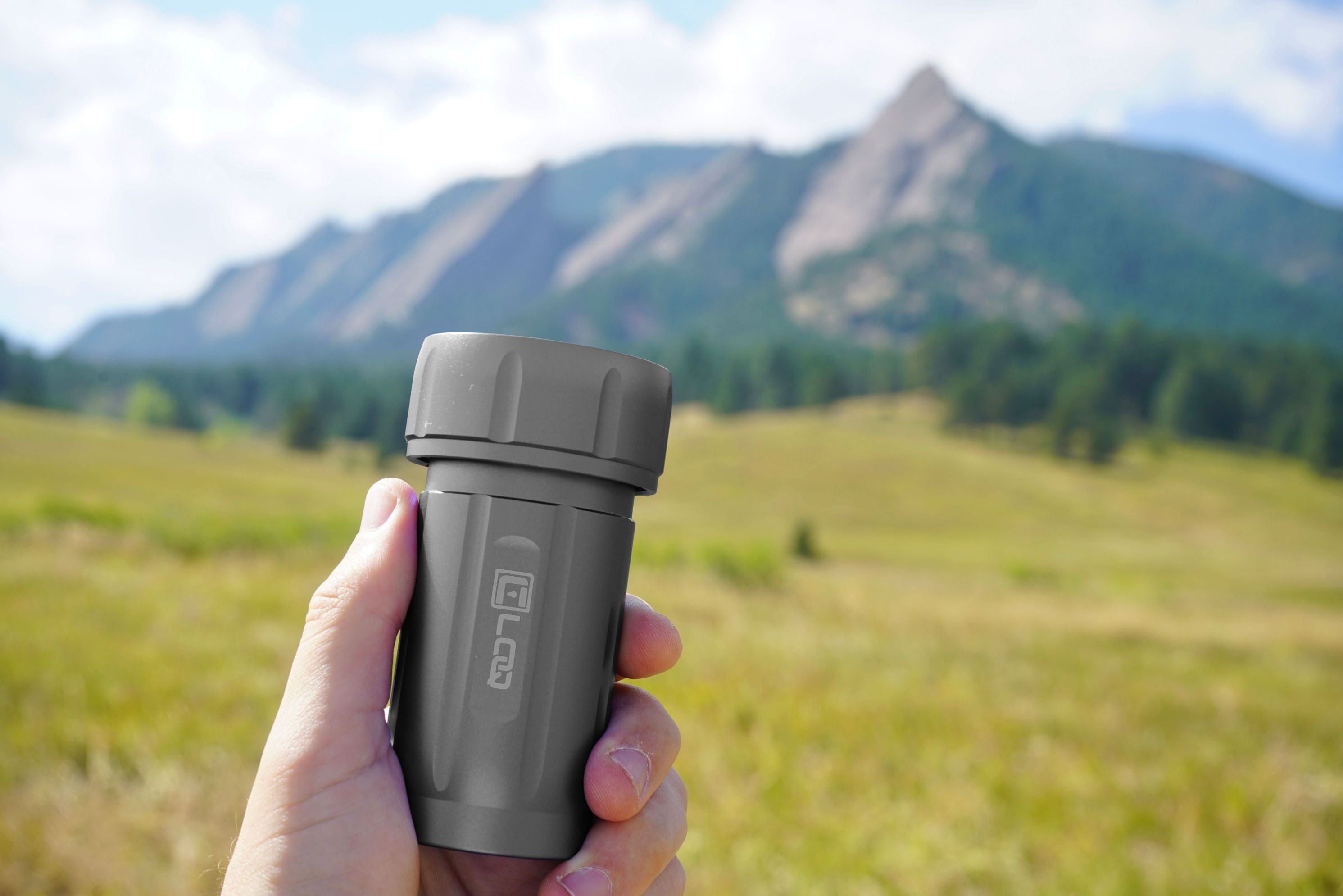 A hand holds the Zytel Gray Premium 120CC Storage Canister against a mountainous, green backdrop.