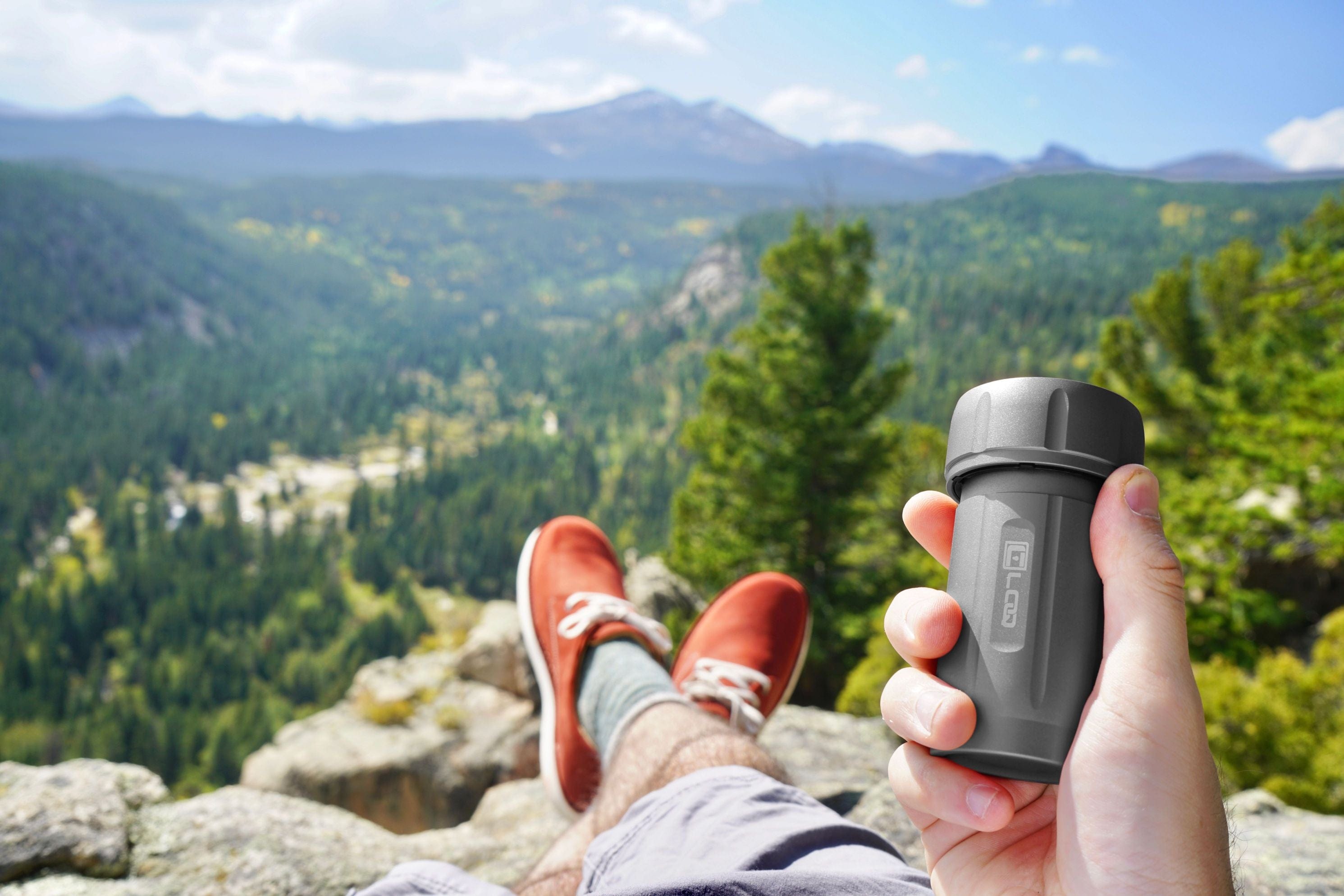 A person’s feet rest near the Zytel Gray Premium 120CC Storage Canister, held against a mountainous backdrop with bright daylight.