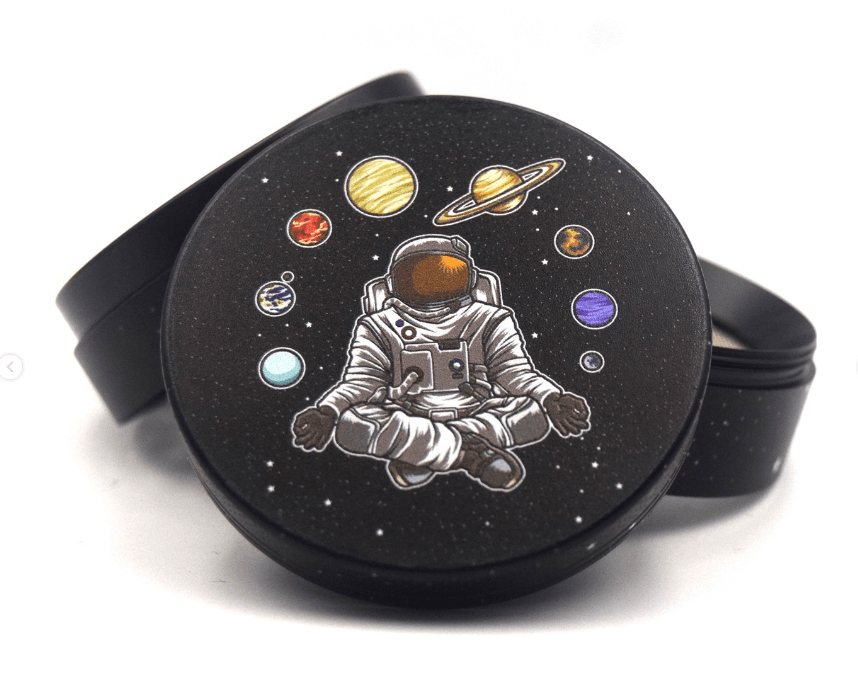 The 4 Piece 2.5" Trip to the Moon Grinder displays an astronaut amid planets in a cosmic, circular design.