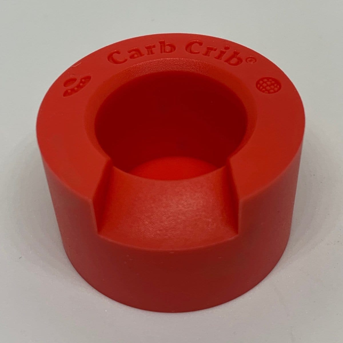 A close-up, angled view of the V2 Carb Crib®, showing its smooth, red surface and simple cylindrical form.