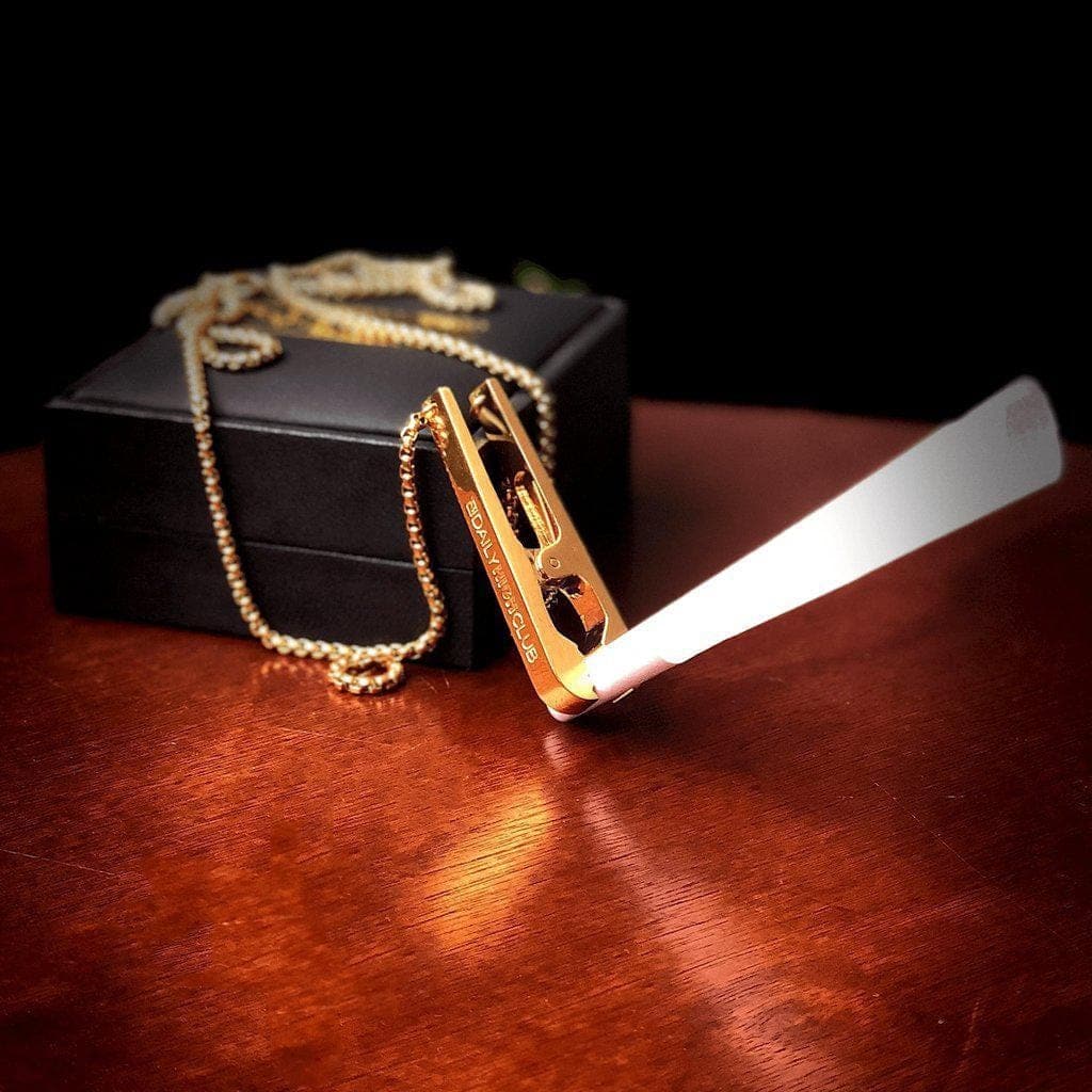 A close-up shows the gold Daily High Club Roach Clip resting on a dark surface with a gold chain nearby.