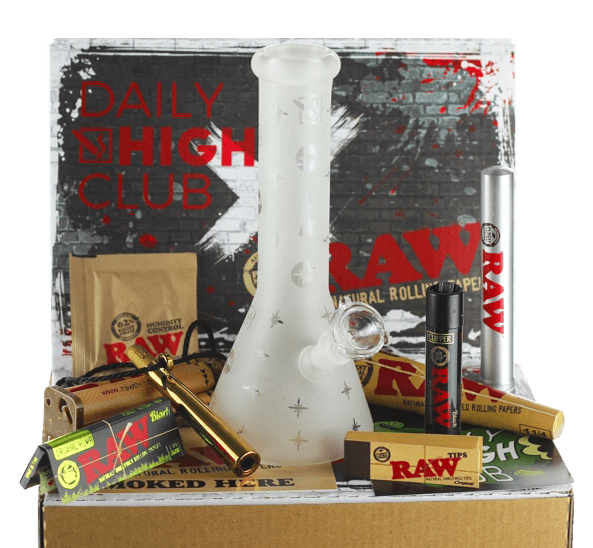 The “RAW x DHC” Smoking Box is pictured from a high angle, showcasing various smoking accessories arranged around a clear glass piece.