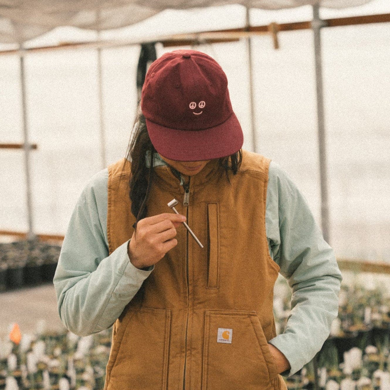 A medium shot shows a person holding the Long Cobb Titanium Pipe, framed by a greenhouse’s soft lighting and lush greenery.