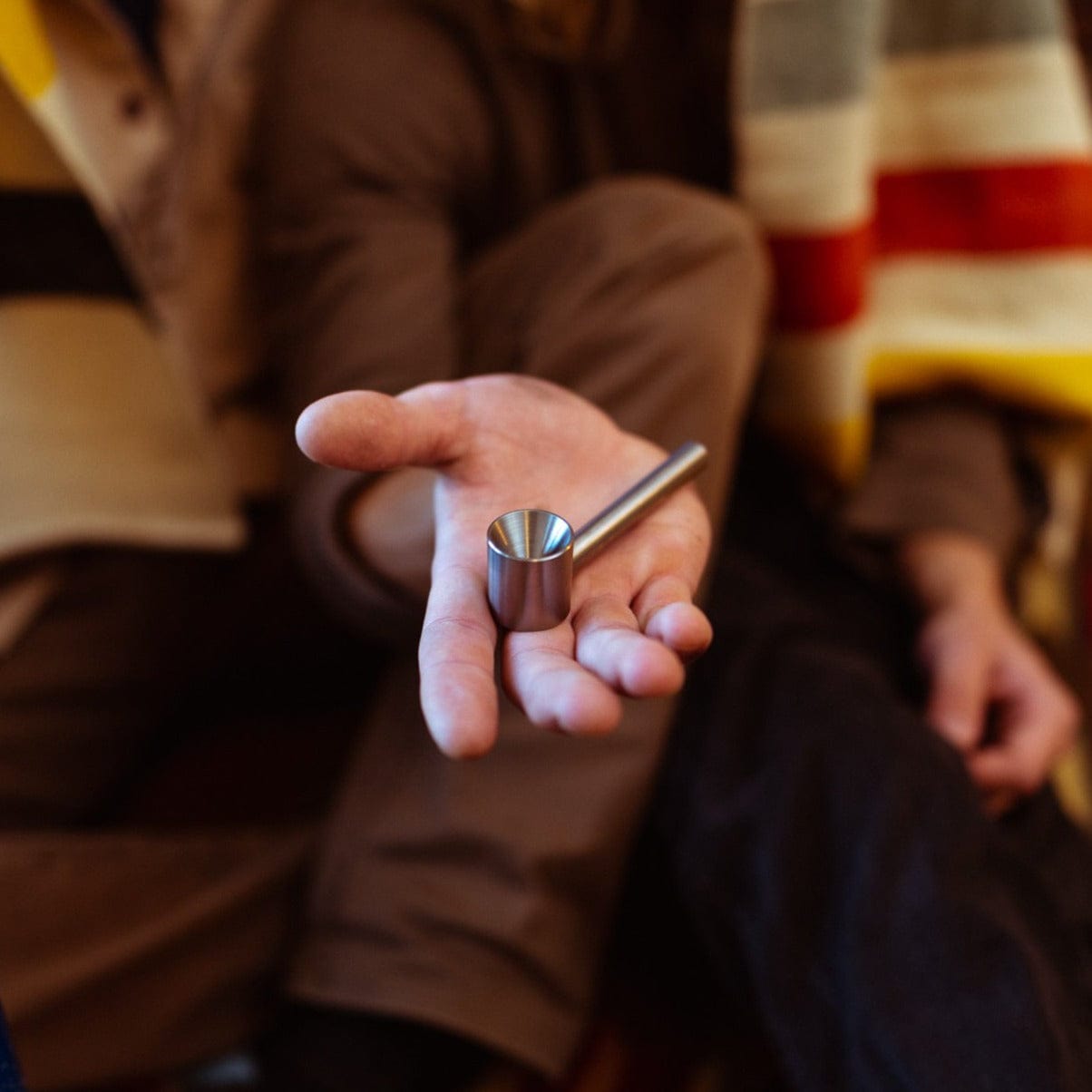 A hand holds the Smokey Pipe Titanium Pipe, showcasing its metallic sheen against a blurred background.