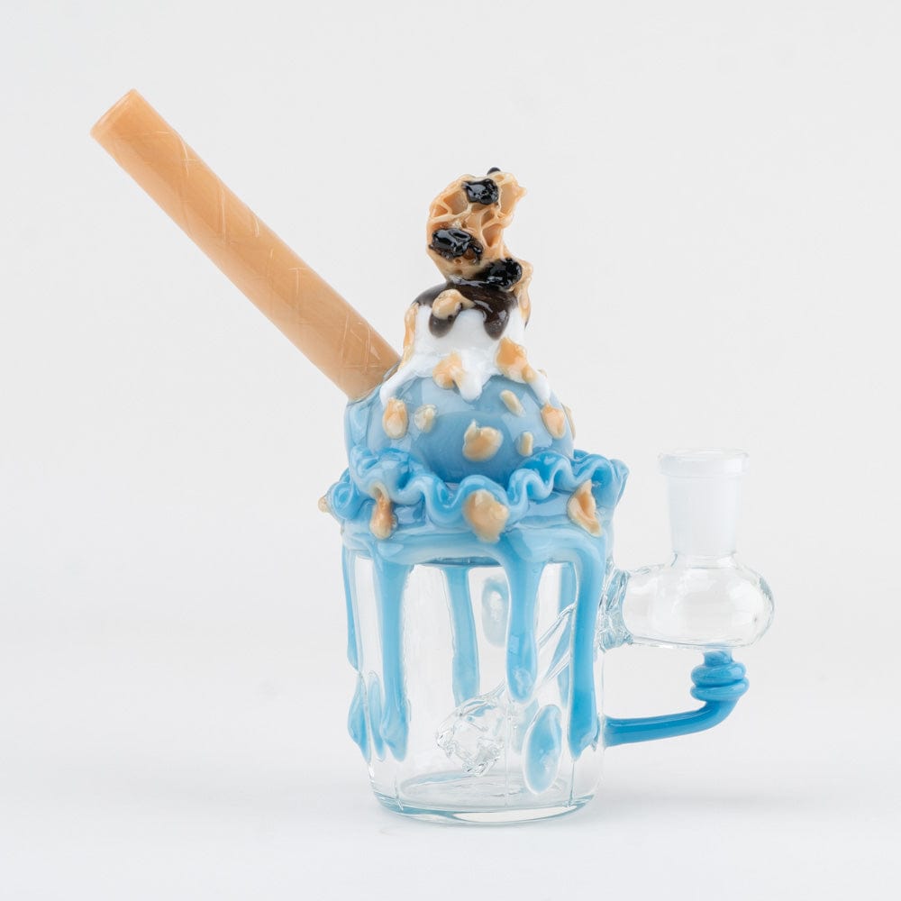Front-facing shot of a glass "Cookie Monster Sundae Nano Rig" topped with blue drippy "ice cream," cookie bits and a beige wafer straw.