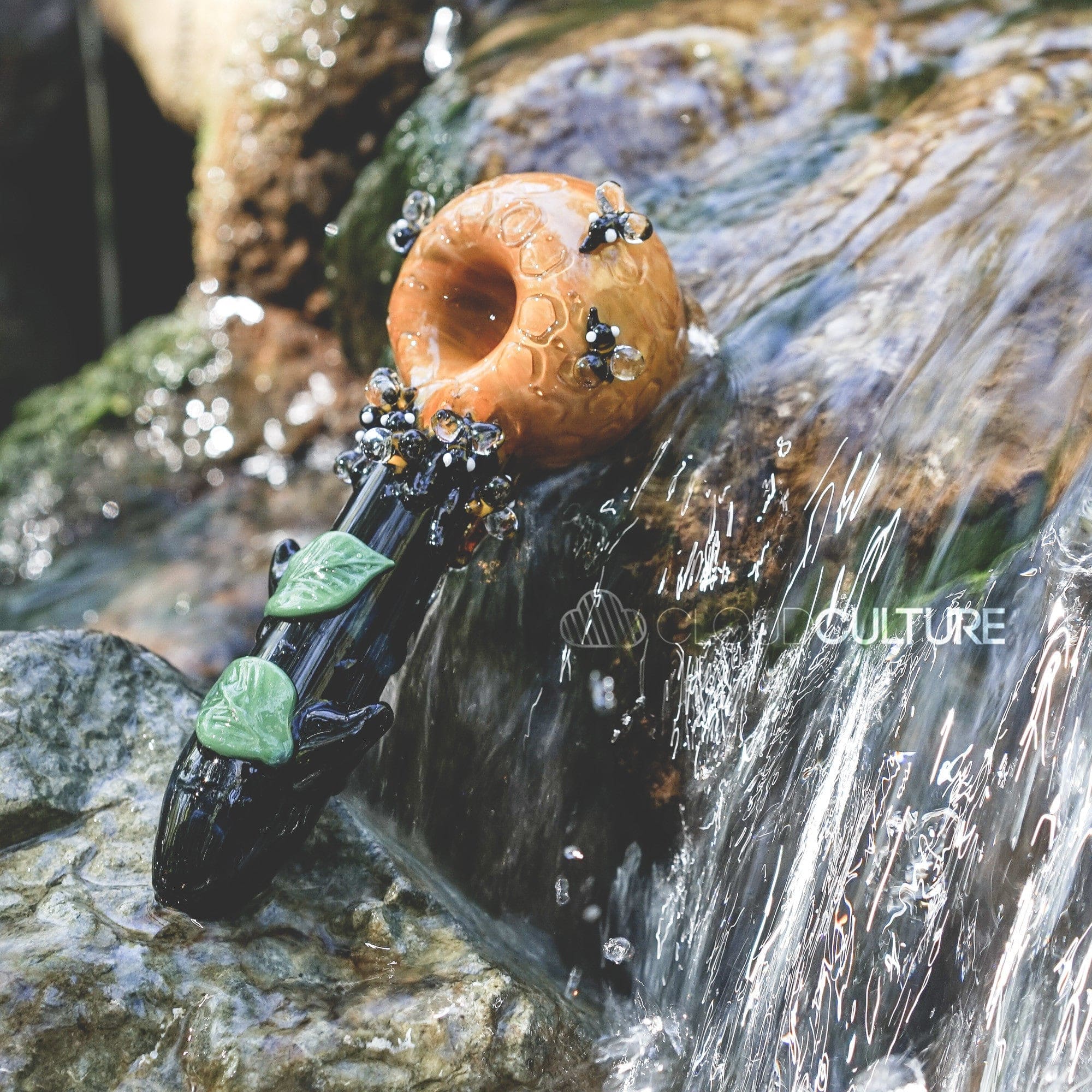 A close-up shot of the Beehive Large Spoon Pipe, partially submerged in clear water with a rocky background.