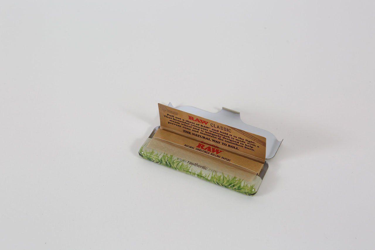 Close-up of the Raw Paper Tin with a metallic sheen and visible branding, positioned against a blurred background.