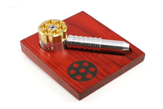 Front view of The Original Six Shooter Pipe resting on a reddish-brown surface, showcasing its metallic details.
