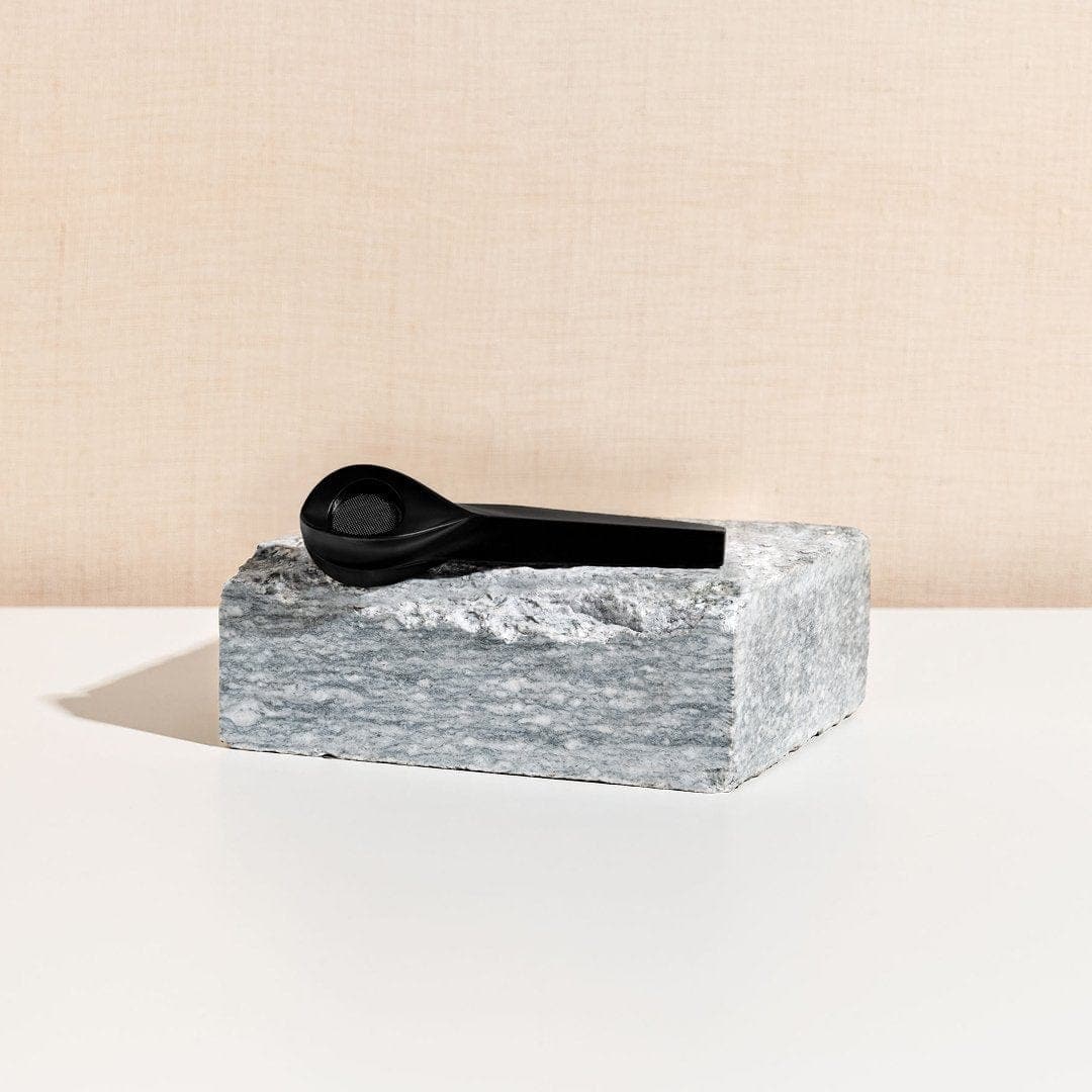 A side view of the KØL Mini 2.0 Titanium Travel Utensil Set resting on a textured gray block.
