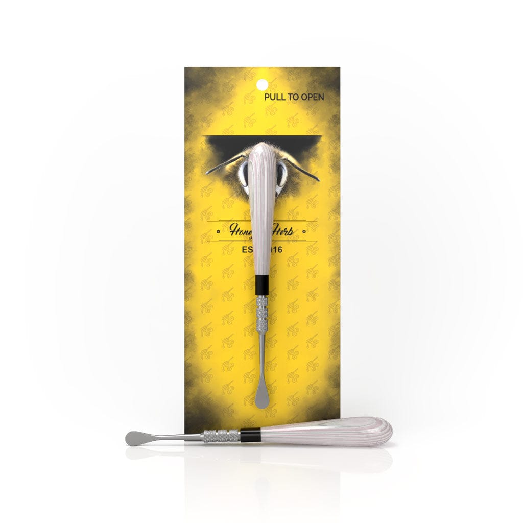 A close-up of the Classic Dab Tool against a yellow background, showing the tool's slender design within packaging.