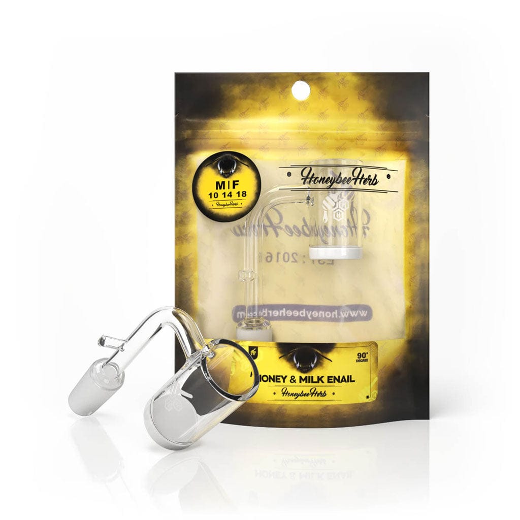 Front three-quarter view of the HONEY & MILK ENAIL QUARTZ BANGER - 90Â° DEGREE | YL resting on a white surface with its clear glass joint and bucket angled before branded yellow-black packaging.