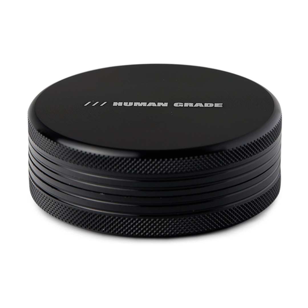 Close-up of the Human Grade Grinder 1C (2.5" 2-Piece) with a textured metallic finish and circular design.