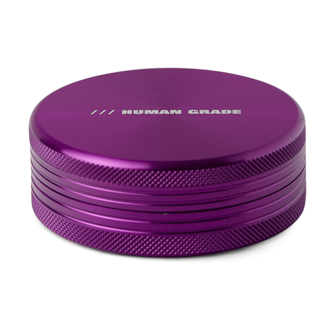 A close-up, angled view of the Human Grade Grinder 1C (2.5” 2-Piece) with a metallic purple finish and textured grip.