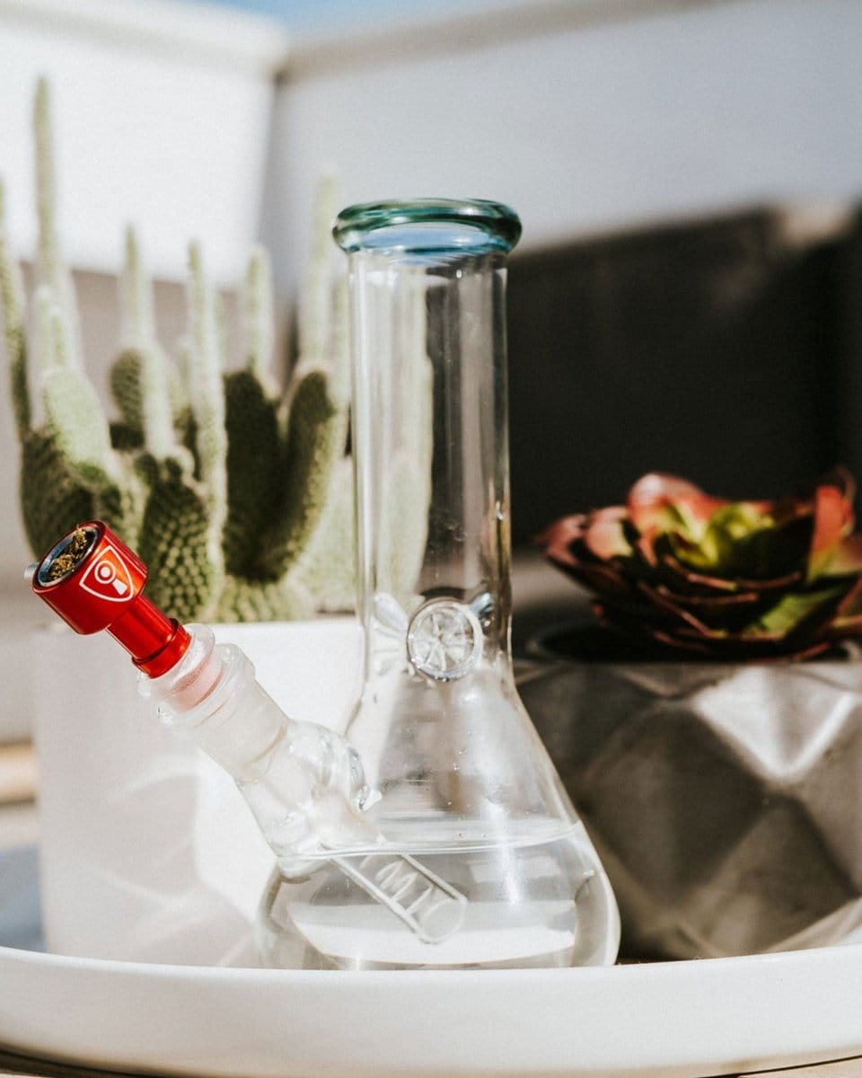 A close-up shows the Indestructible Bong Bowl against a blurred background of plants and a white surface.