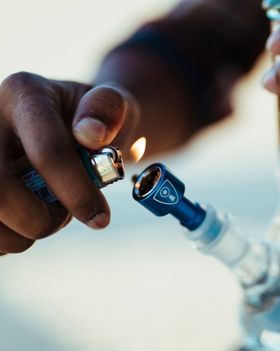 A close-up shot shows a hand lighting the Indestructible Bong Bowl, highlighting its connection point with a flame.