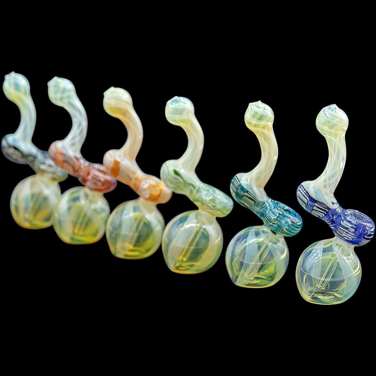 A studio shot displays several colorful “Rake Bubb” Fumed Sherlock Bubbler Pipes arranged against a black background.