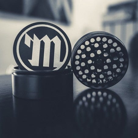 Close-up view of the Myster 4-Piece Grinder with a dark metallic finish, showing its textured grinding surfaces and circular design.