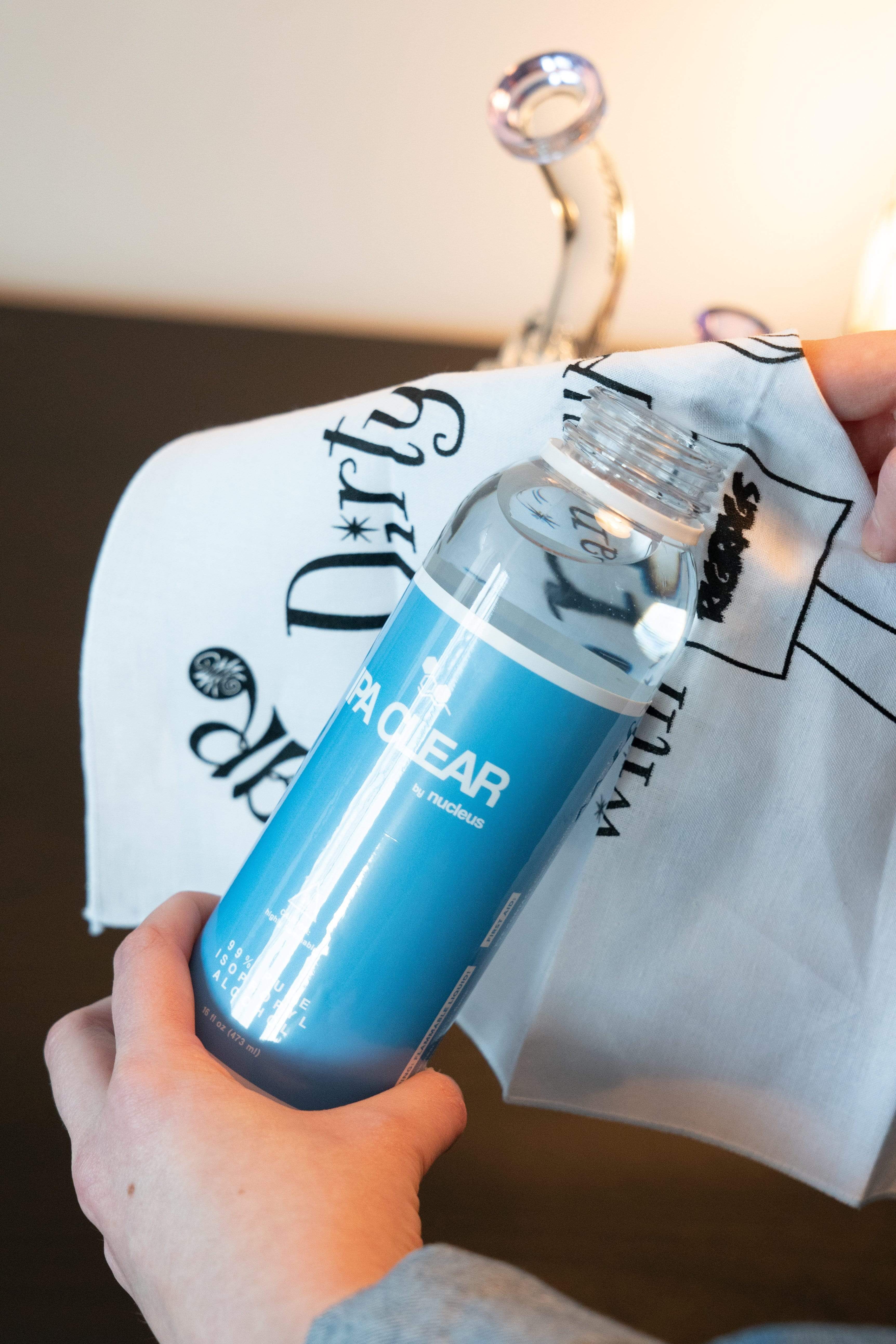 A close-up, slightly angled view of the Pure Isopropyl Alcohol container with visible text against a blurred, patterned background.