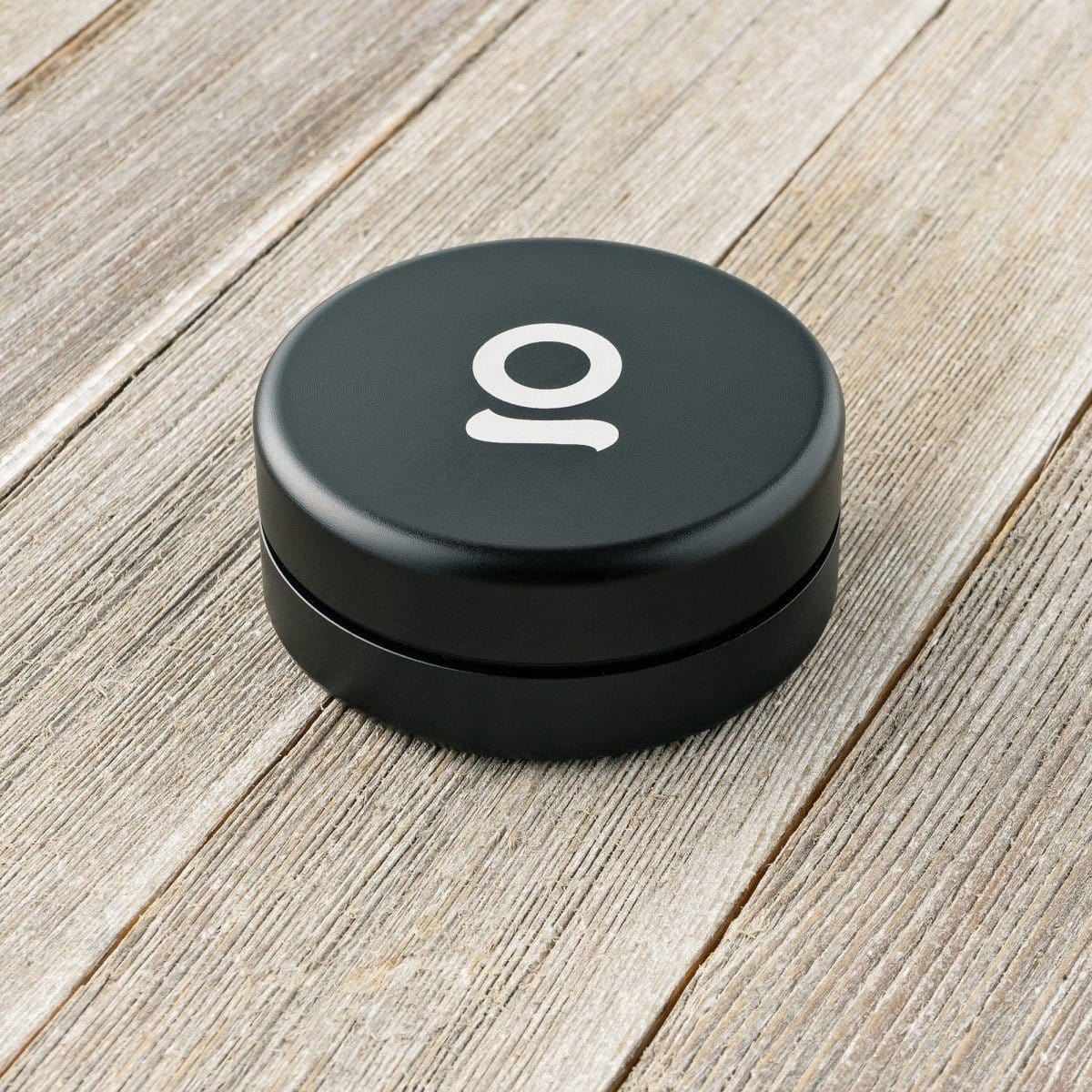 A top-down view of the Aluminium Storage Puck resting on a light wood grain surface, showing its minimalist circular design.