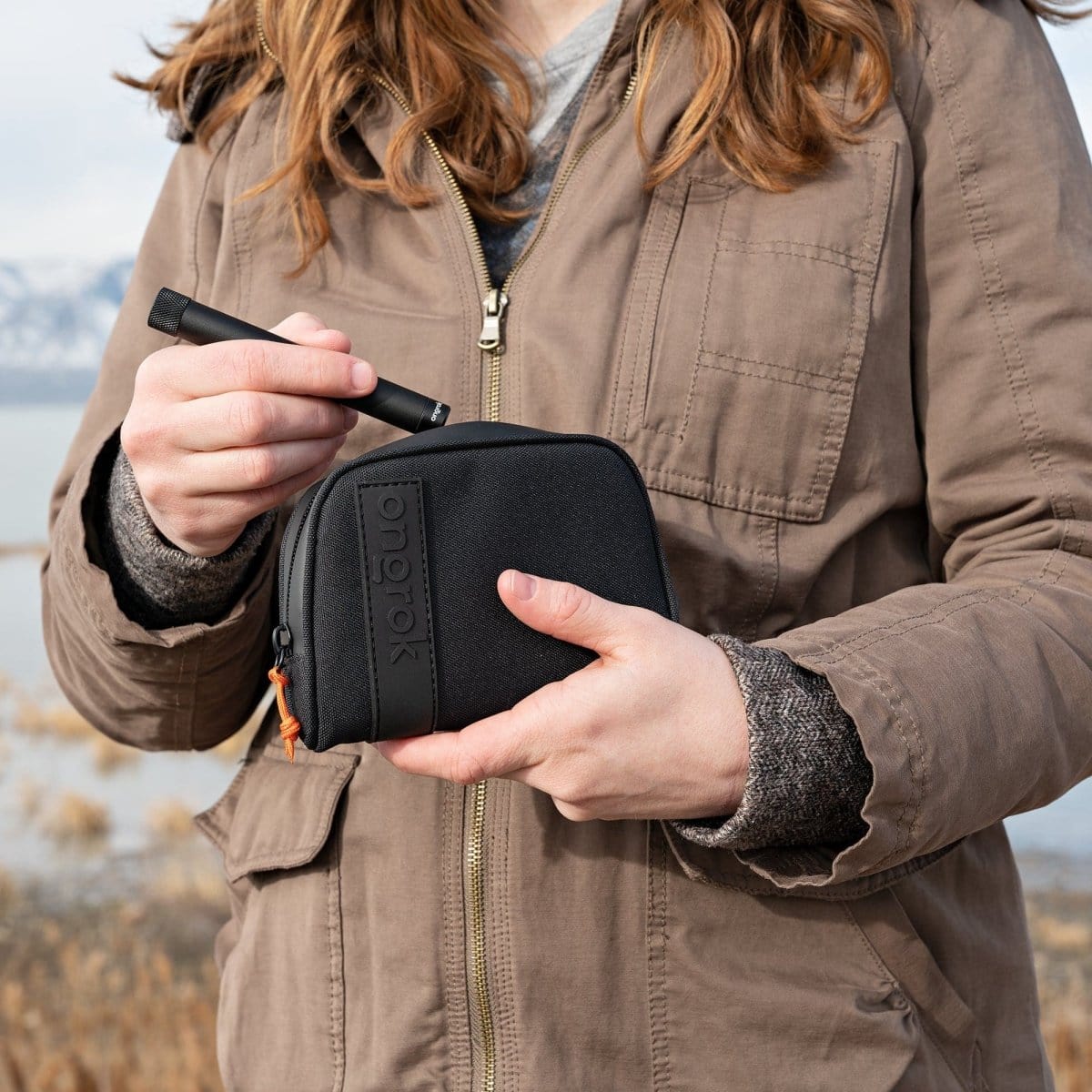 A person holds the Carbon-lined Wallets with Combination Lock V 2.0| viewed from the front and partially obscured by a tan jacket.