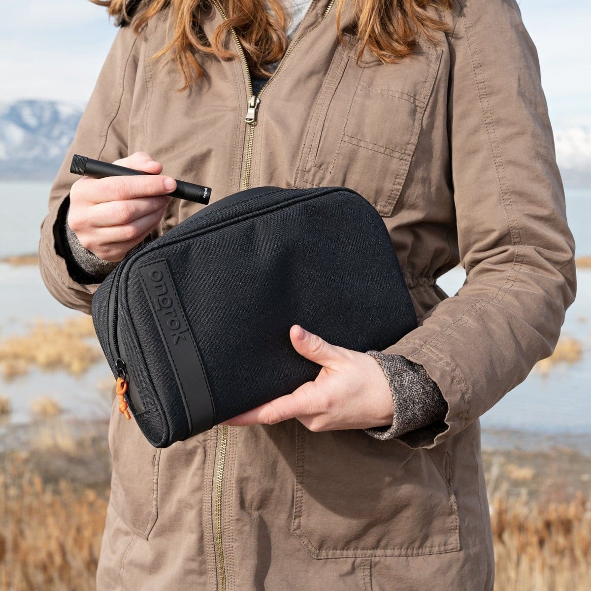 A medium-sized Carbon-lined Wallets with Combination Lock V 2.0 held in hand against a blurred, natural landscape backdrop.