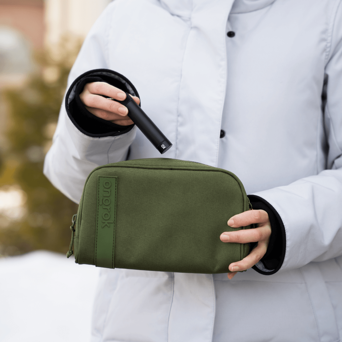 A hand holds the Carbon-lined Wallets with Combination Lock V 2.0 against a blurred outdoor backdrop, showcasing its sleek, rectangular form.