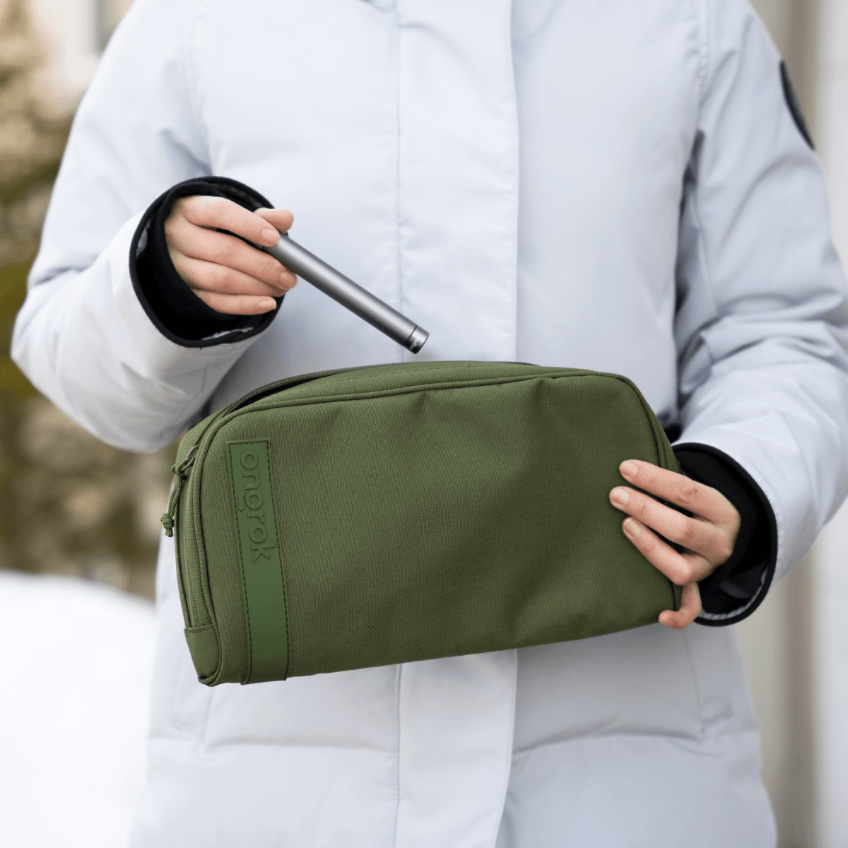 A hand holds the Carbon-lined Wallets with Combination Lock V 2.0 against a winter background, showcasing its sleek, rectangular shape.