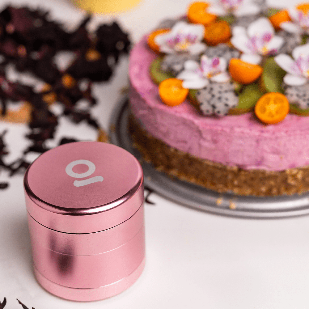 A close-up of the four-piece Premium 4 Piece EZ Grinder, with a silver finish, beside a slice of decorated cake.