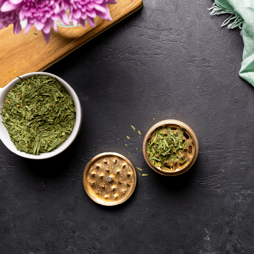 Overhead view of the Premium 4 Piece EZ Grinder with a silver finish, next to a small bowl of green herb.