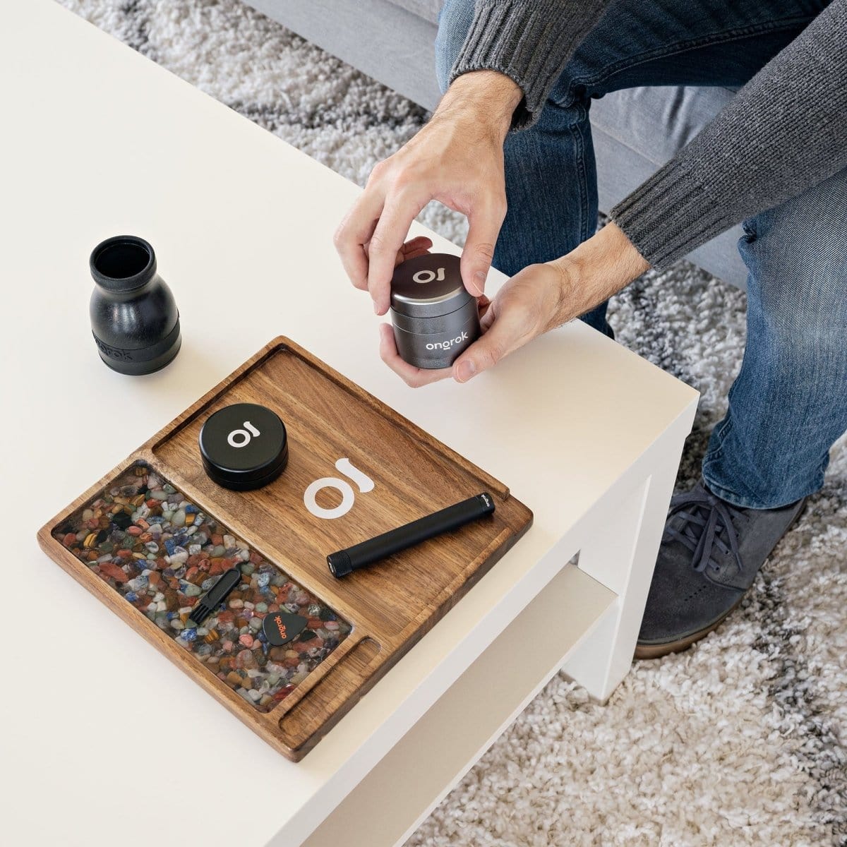 A hand holds the Premium 4 Piece EZ Grinder, positioned next to a second grinder on a light wood surface.