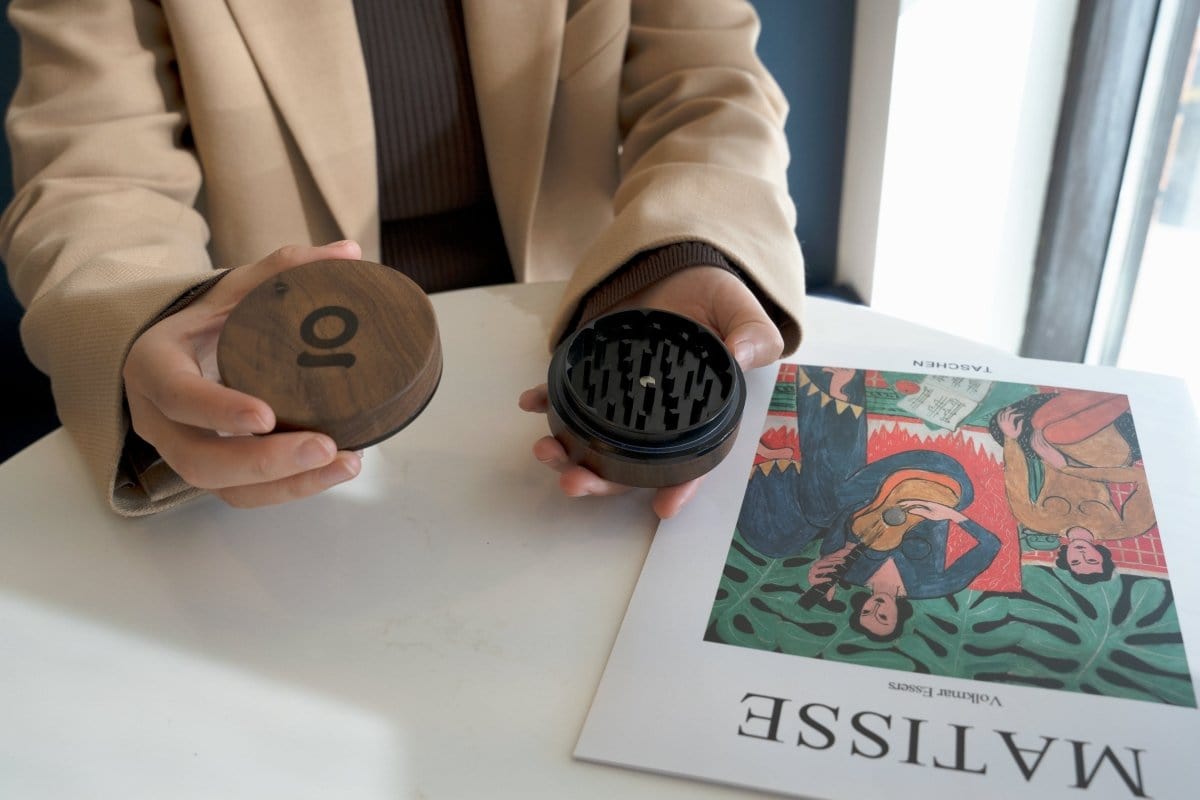 A close-up, angled view showcases the 3 Inch, 2-Piece Walnut Grinder held in a person’s hand against a patterned backdrop.
