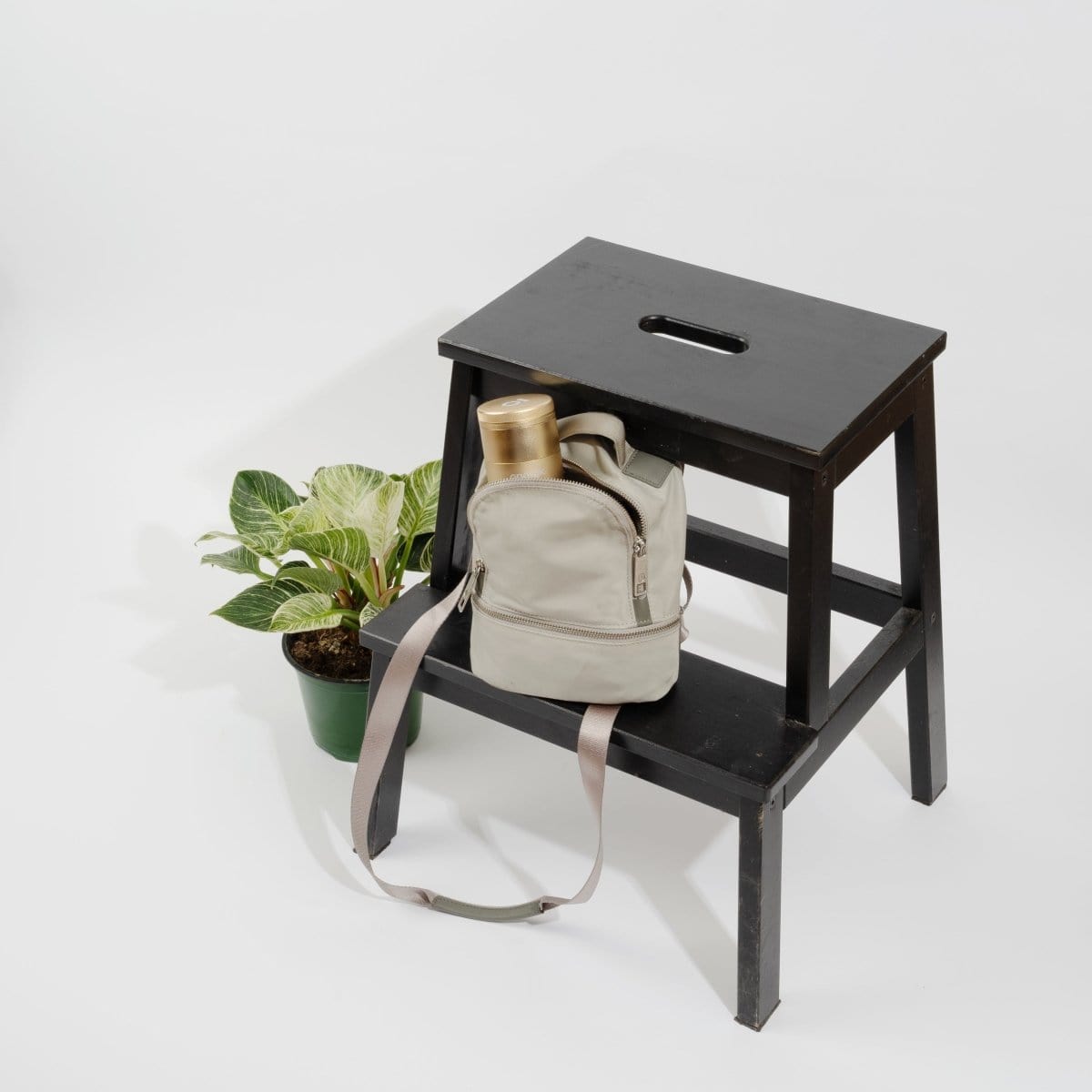 A high-angle view shows the 5 Piece Storage Grinder resting on a wooden stool beside a potted plant.