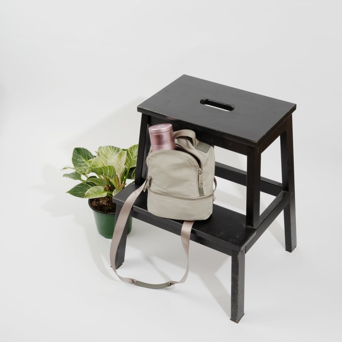 A high-angle view of the 5 Piece Storage Grinder placed on a wooden stool next to a potted plant.