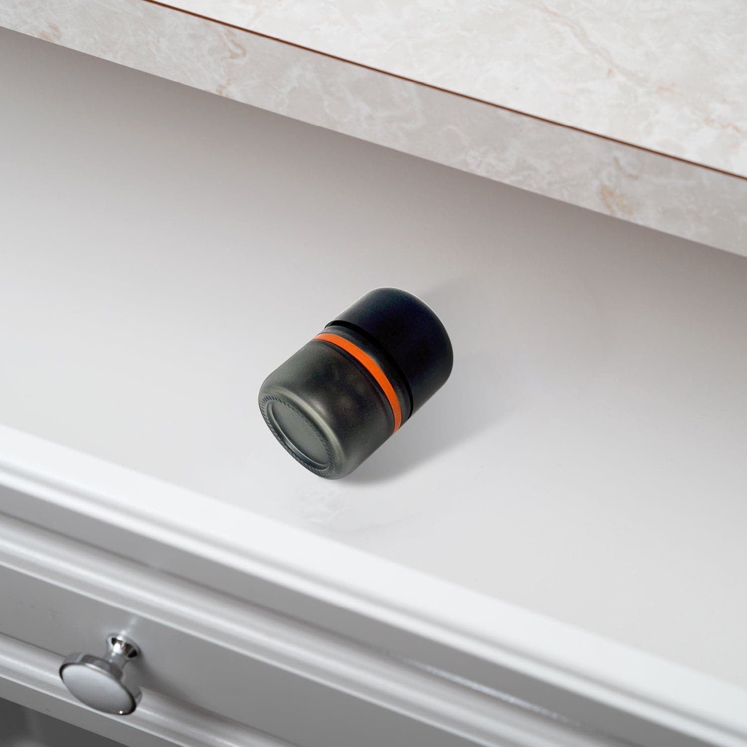 Angled close-up of an 80ml Child Resistant Jar | 6 Pack resting on a white tabletop, showing its matte black lid, smoked glass body and orange seal.