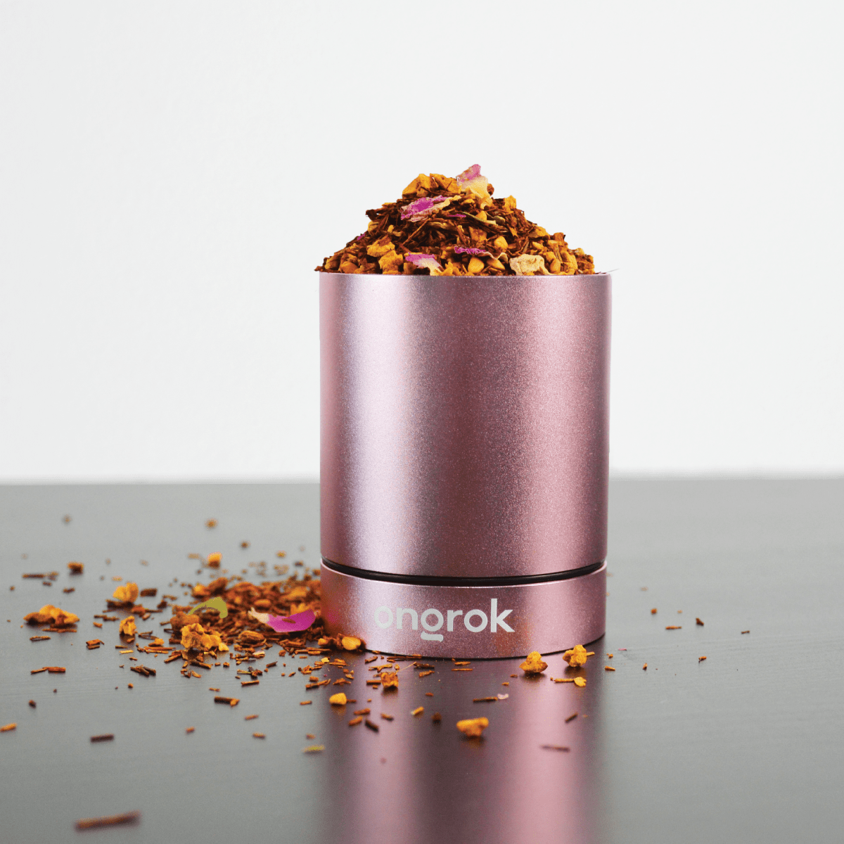 A front view of the Aluminum Metal Storage Jar, reflecting light on its smooth surface amidst scattered plant matter.