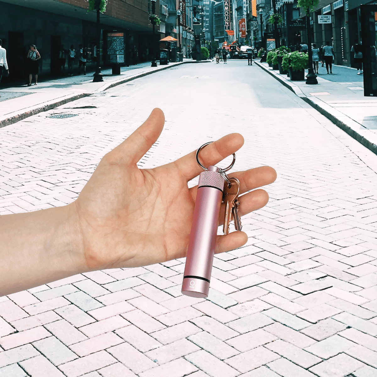 A hand holds the Aluminum Storage Keychain amidst a blurred city street scene with a low-angle perspective.