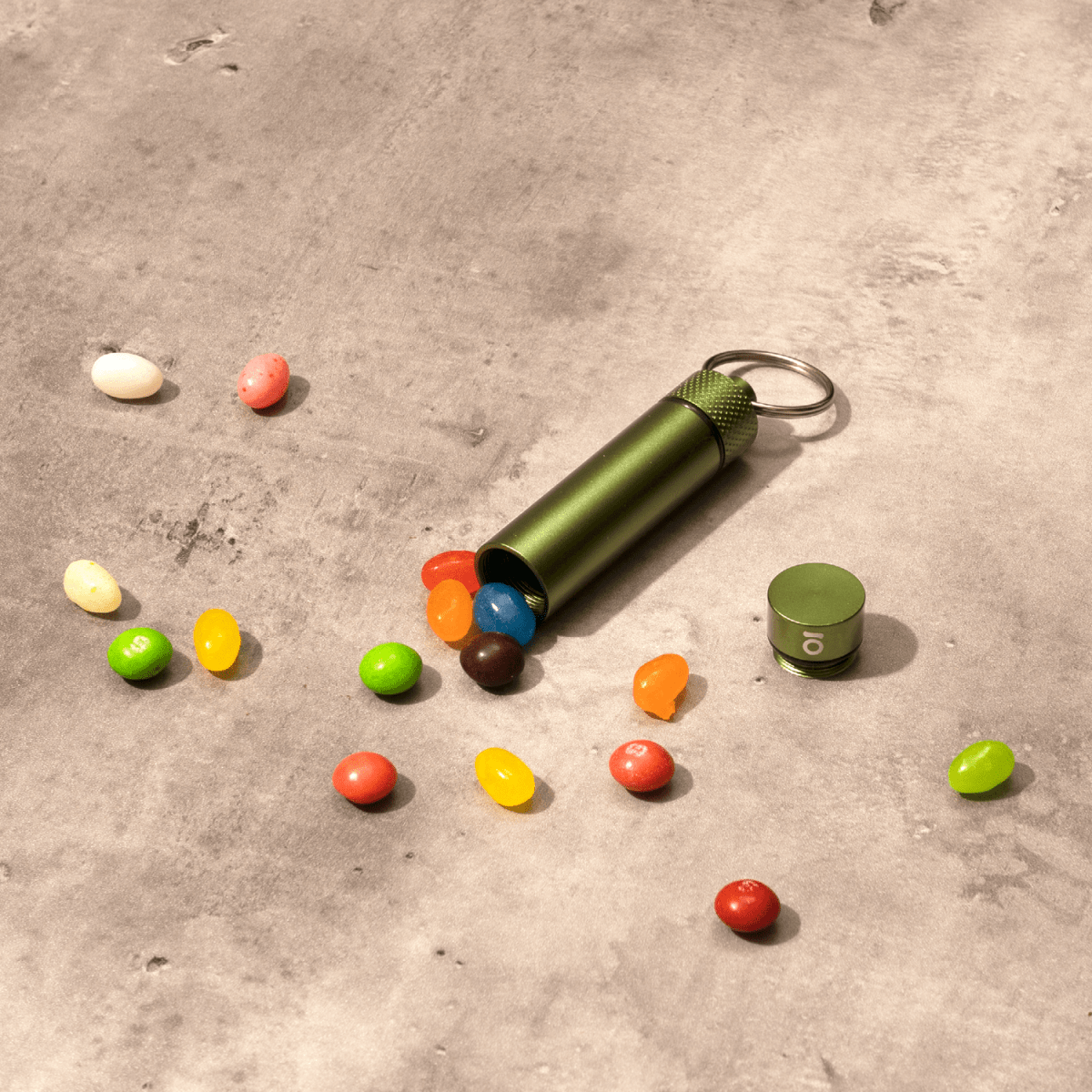 Overhead shot of the Aluminum Storage Keychain alongside colorful candies on a textured gray surface.