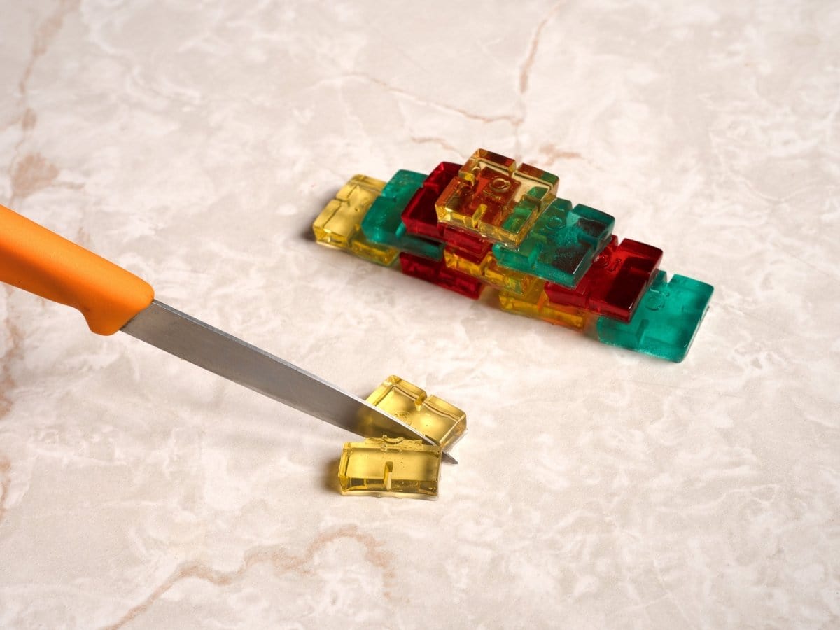 A top-down view of scored gummy molds in vibrant colors, positioned alongside a silver knife on a textured surface.