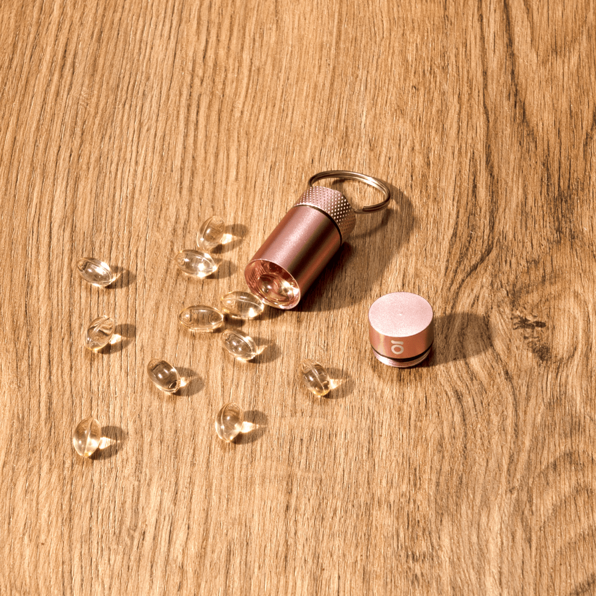 Overhead view of the Small Storage Keychain, a silver-toned cylinder surrounded by clear, faceted gems on a wood surface.