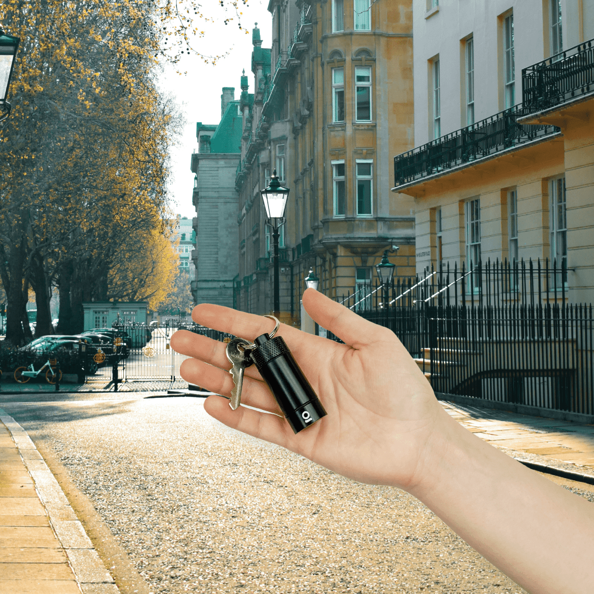 A hand holds the Small Storage Keychain against a blurred background of a city street and historic buildings.