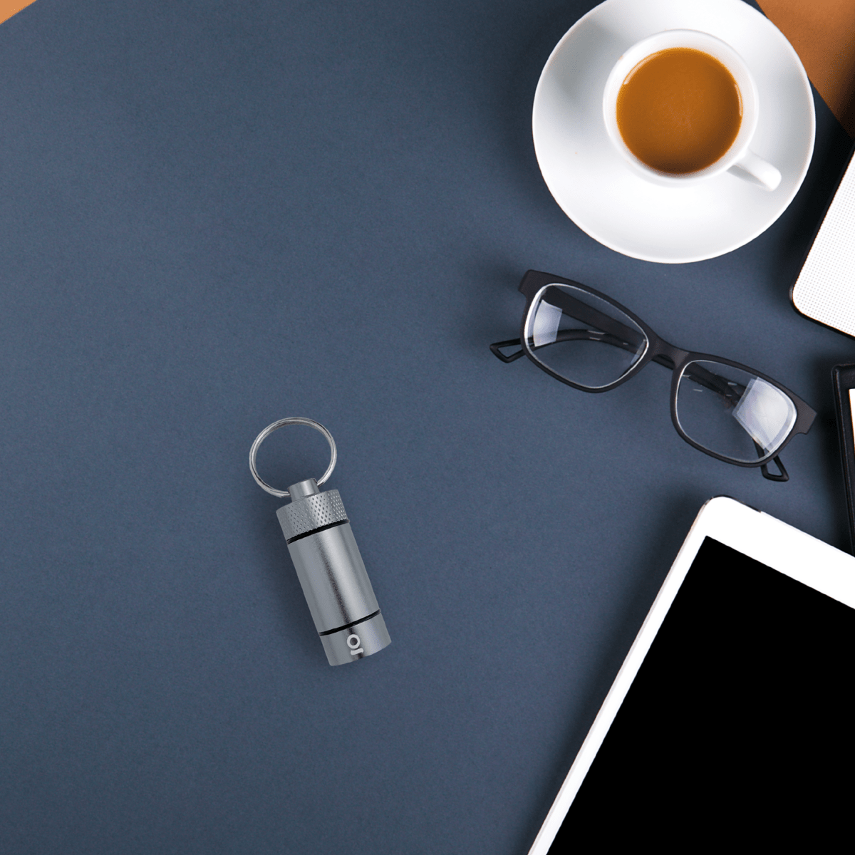 Top-down view of the Small Storage Keychain resting beside glasses and a coffee cup on a blue surface.