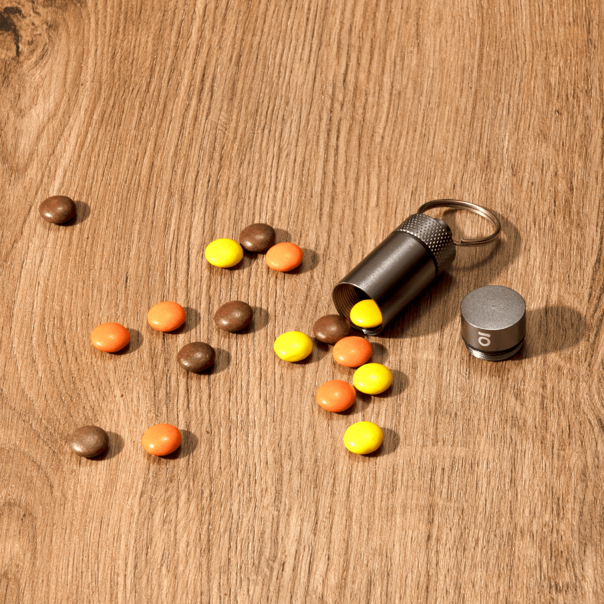 A high-angle view of the Small Storage Keychain amidst colorful candies on a wooden surface.