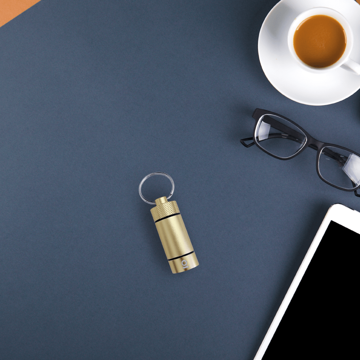 Overhead view of the Small Storage Keychain next to a coffee cup and eyeglasses on a dark surface.