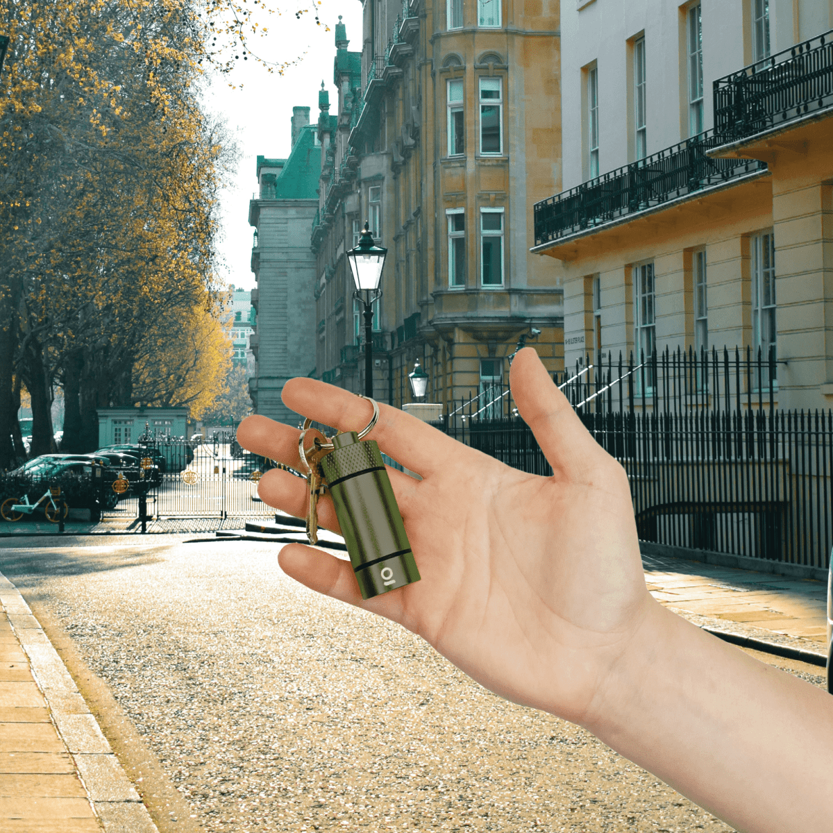 A hand holds the Small Storage Keychain against a blurred cityscape backdrop, showcasing its compact size and metallic finish.